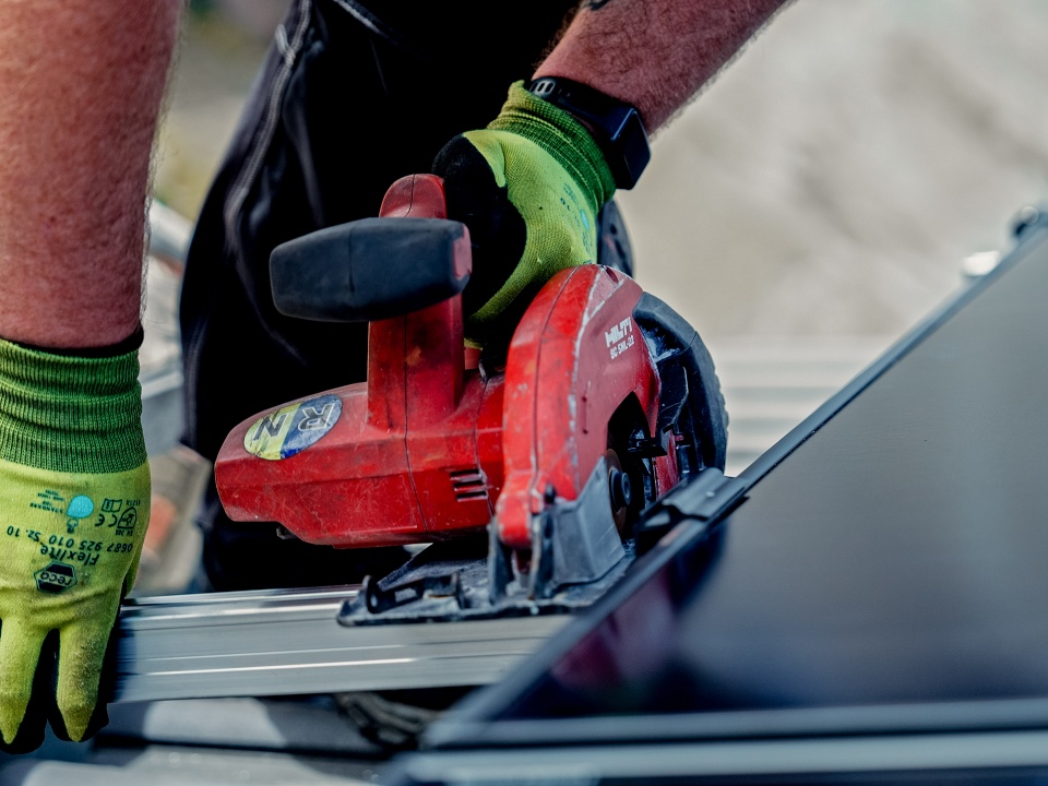Eine Person mit gr&uuml;nen Handschuhen schneidet Metall mit einer roten Kreiss&auml;ge und denkt &uuml;ber Projekte wie &bdquo;Solaranlage Mieten &ndash; Lohnt Sich Das?&ldquo; f&uuml;r nachhaltige Modernisierungen nach.